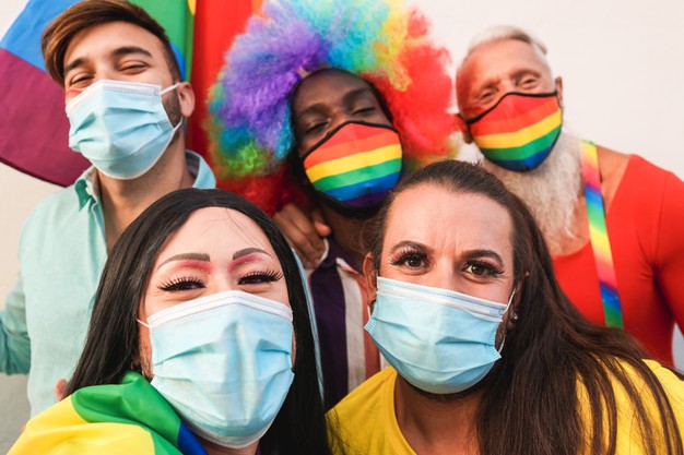 A imagem mostra um grupo de pessoas durante a parada LGBT, usando máscaras de proteção contra o coronavírus.