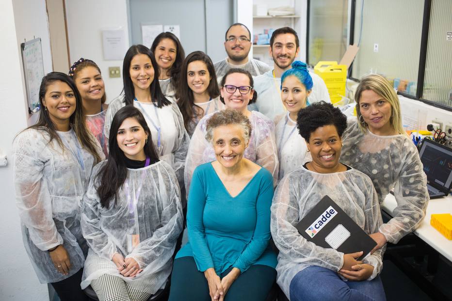 A imagem é uma foto da equipe que sequenciou o genoma do coronavírus no Brasil, em 2020, liderada pela cientista Jaqueline Góes de Jesus, também presente na foto.