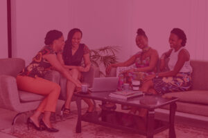 A imagem mostra um grupo de mulheres negras conversando ao redor de uma mesa.