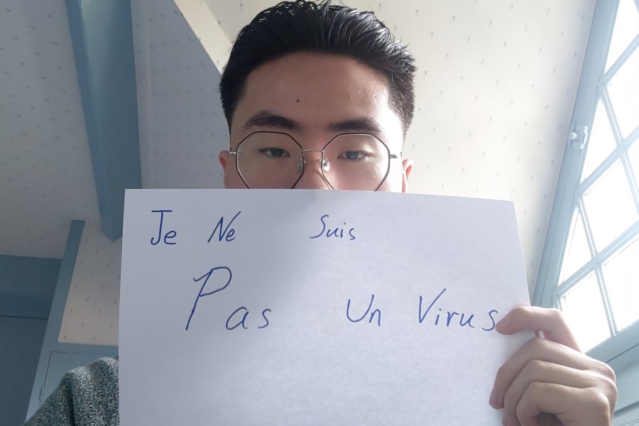A imagem mostra um homem asiático segurando uma placa escrito "Je se suis pas un virus" ("Eu não sou um vírus", em português)