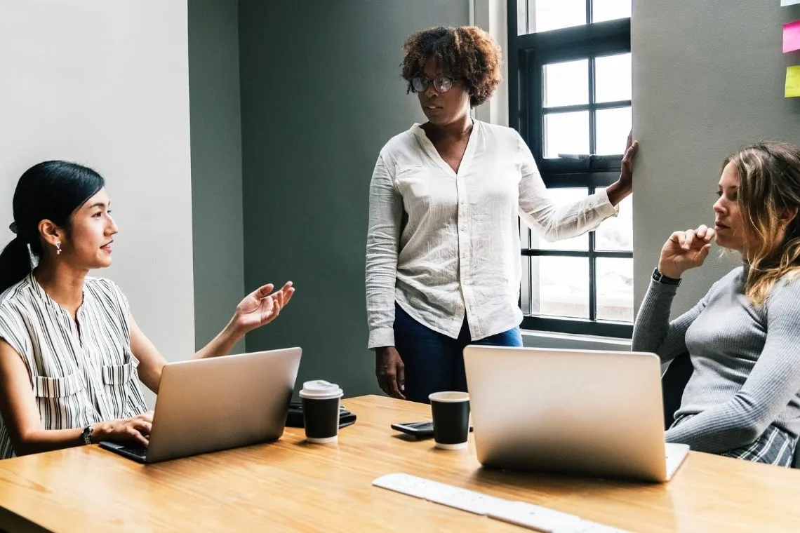 Três mulheres reunidas em uma mesa de escritório corporativo