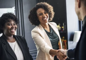 Duas mulheres negras vestidas formalmente e cumprimentando outra pessoa.